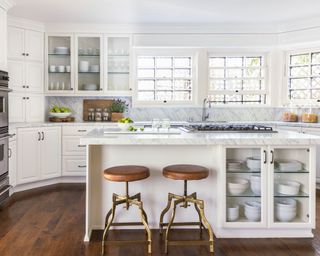 White kitchen island with glass-front cabinets and leather-topped round stools
