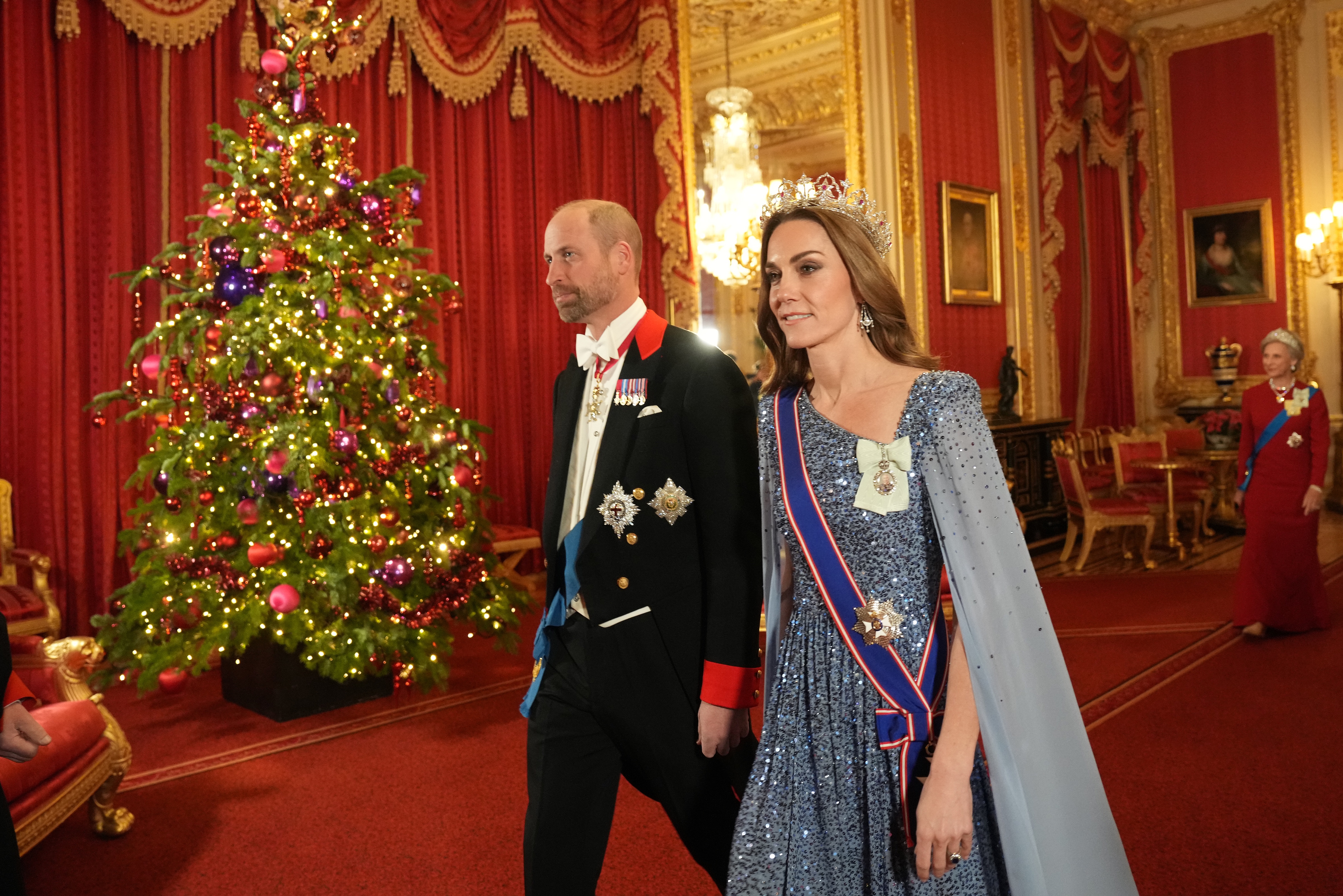 Kate Middleton and Prince William walking past a Christmas tree in formalwear