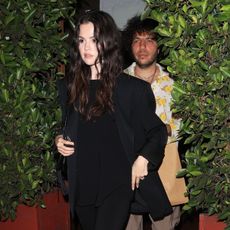 Selena Gomez wearing a black blazer, black cropped pants, and kitten-heel thong sandals with Benny Blanco