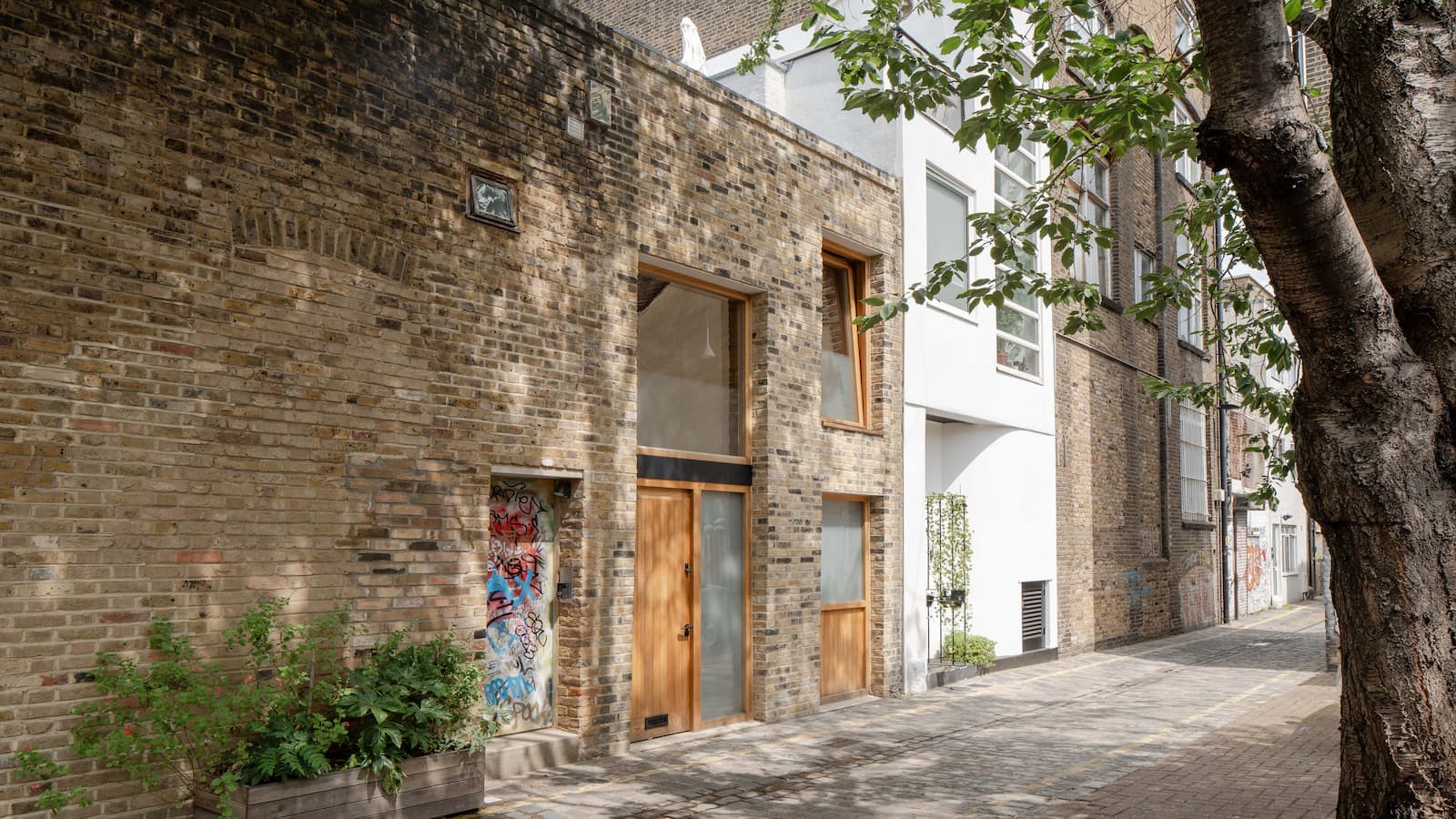 A brick exterior of a terraced house with a tree outside the front door