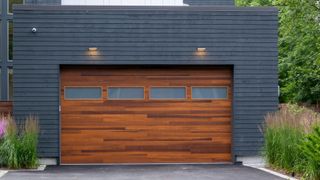 A wooden garage door on a grey clad garage with a flat roof and grey tiled driveway