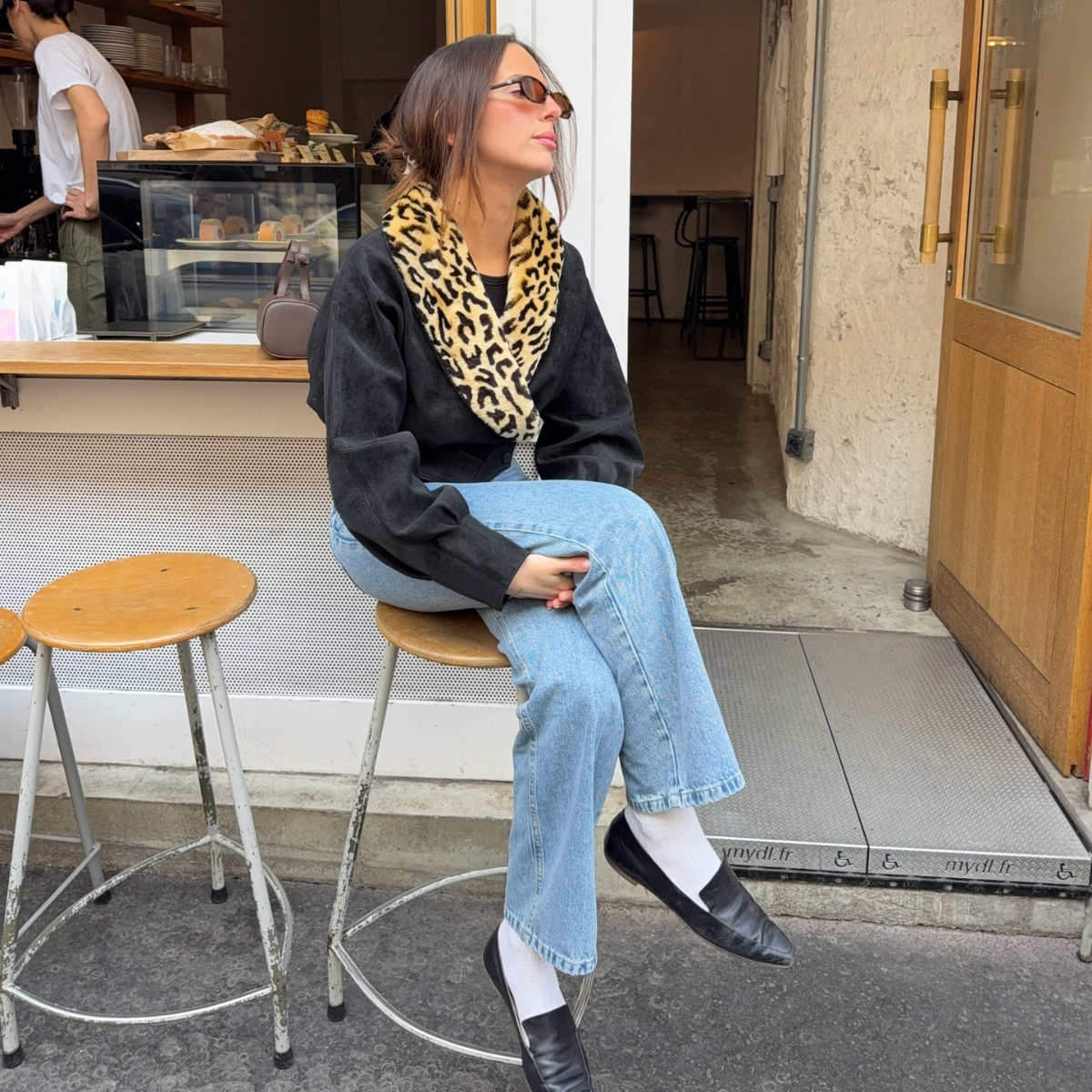 An image of an influencer wearing a black coat with a faux leopard print collar, light blue jeans and black loafers in Paris