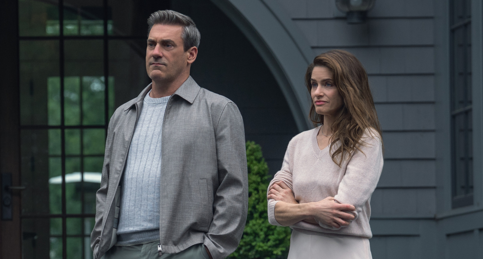 amanda peet folds her arms as mel standing next to jon hamm as coop outside of their home in the season 2 finale of your friends and neighbors