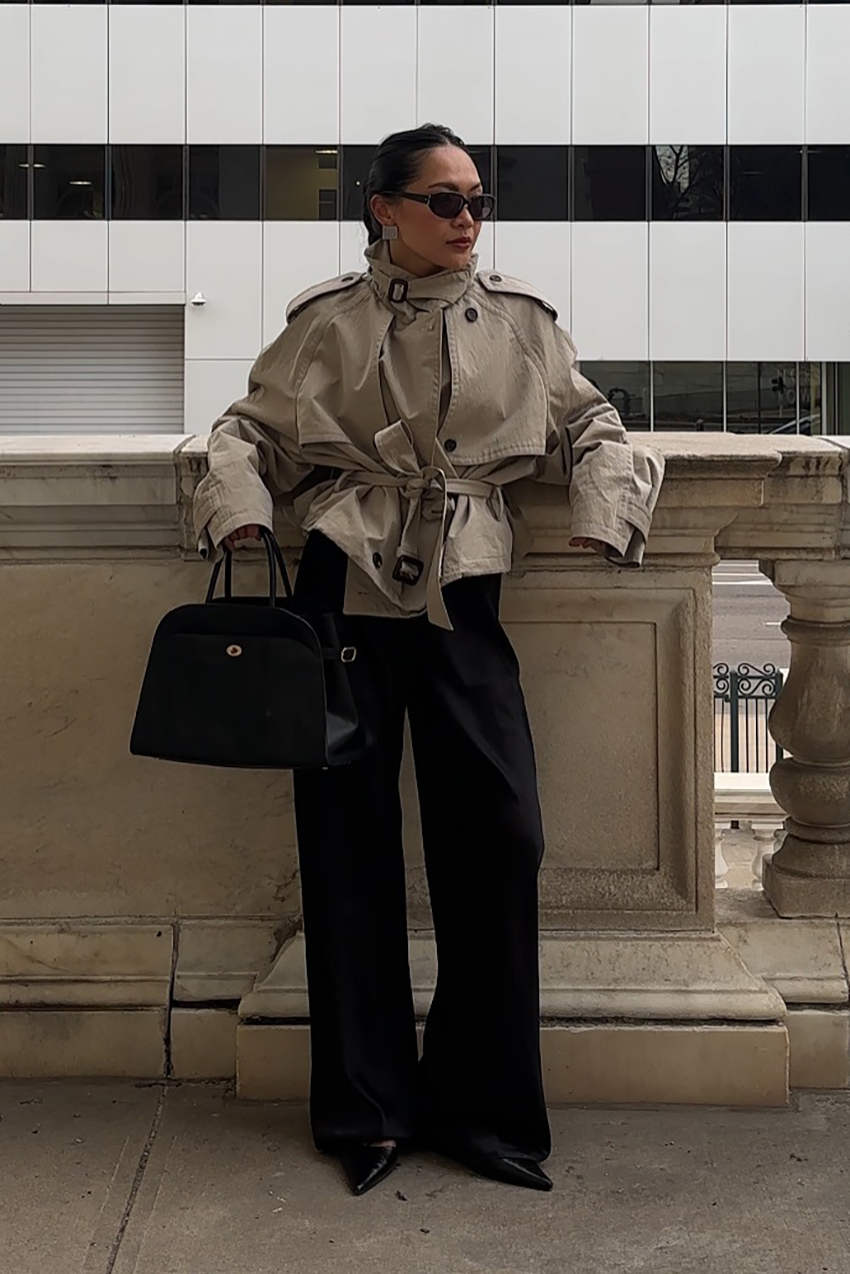 a woman wearing a cropped trench coat, black pants, black pointed toe heels, and a black handbag