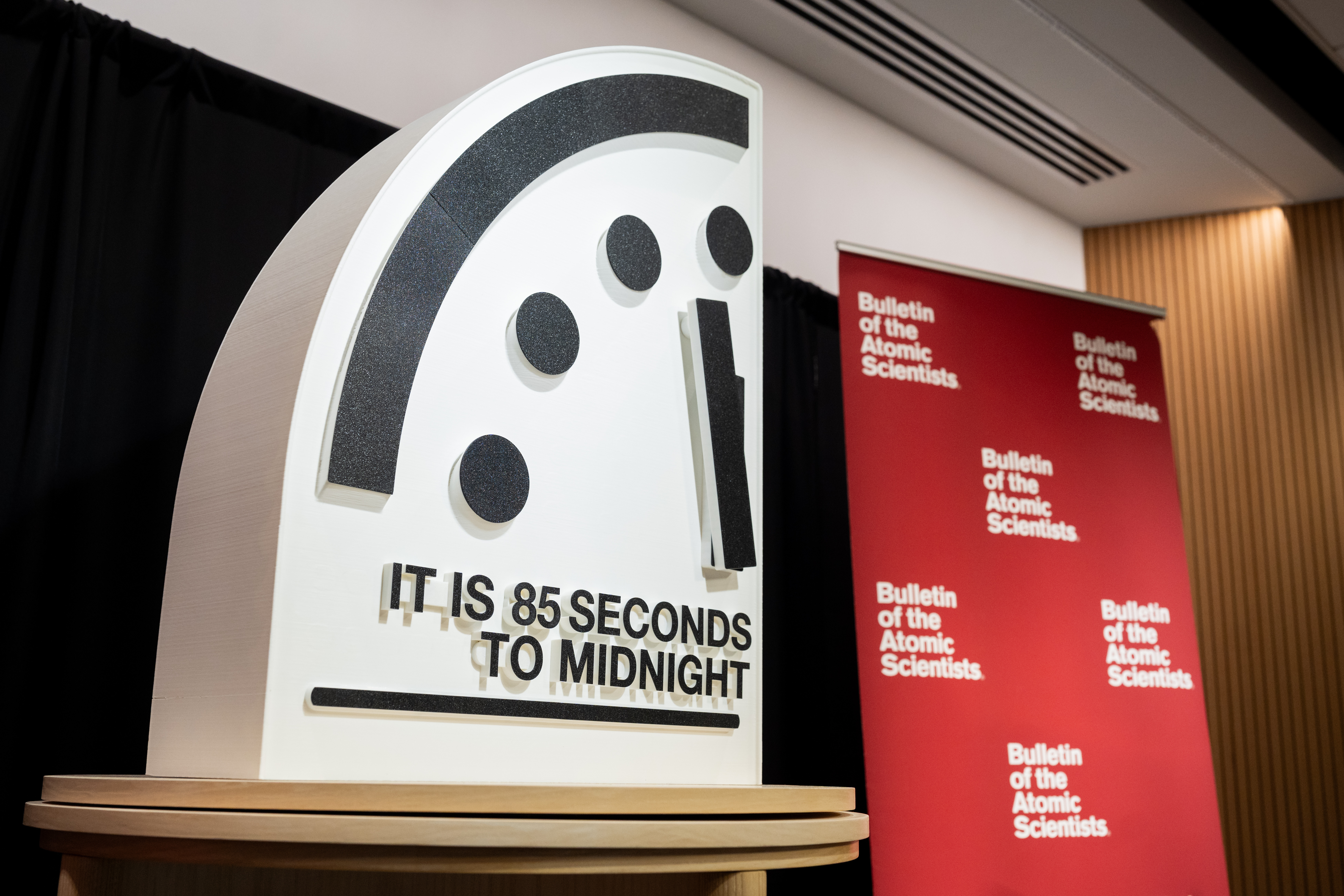 A physical three-dimensional model of the Doomsday Clock showing "85 seconds to midnight" set against a backdrop of Bulletin of the Atomic Scientists banners.