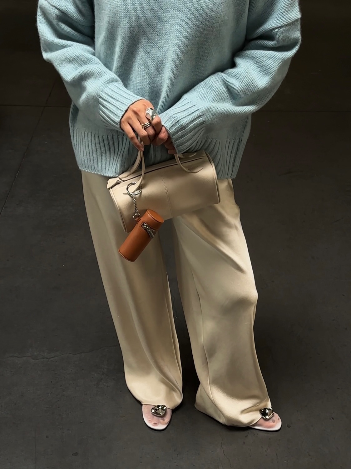 An image of an influencer wearing a teal wool jumper with champagne-coloured satin trosuers and white mesh flats whilst carrying a cream baguette bag