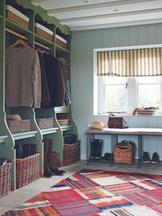 An example of mudroom ideas showing a brightly patterned floor rug and green storage with wicker baskets