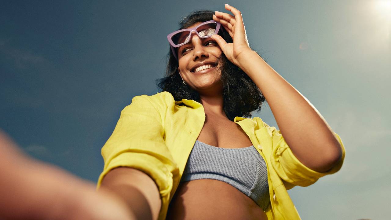 A happy woman looking away holding a pair of square sunglasses. 