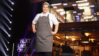 Contestant Kelly in a white top and grey apron in front of the kitchen in Next Level Chef.