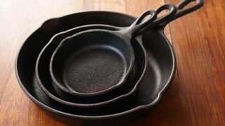 Three empty cast iron skillets stacked on a wooden surface