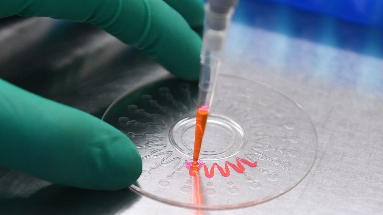 A technician demonstrating how to inject a nucleic acid sample onto a disk for analysis, in a lab 