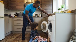 Man and his toddler bending down to use the washing machine in kitchen.