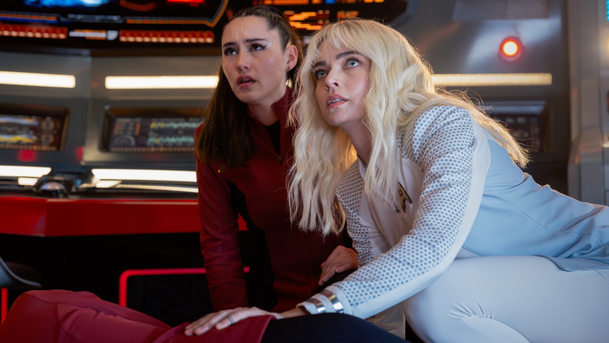 La'an and Christine lay over an injured Scotty, Chapel is wearing a white uniform, and La'an her red. They both look worried.