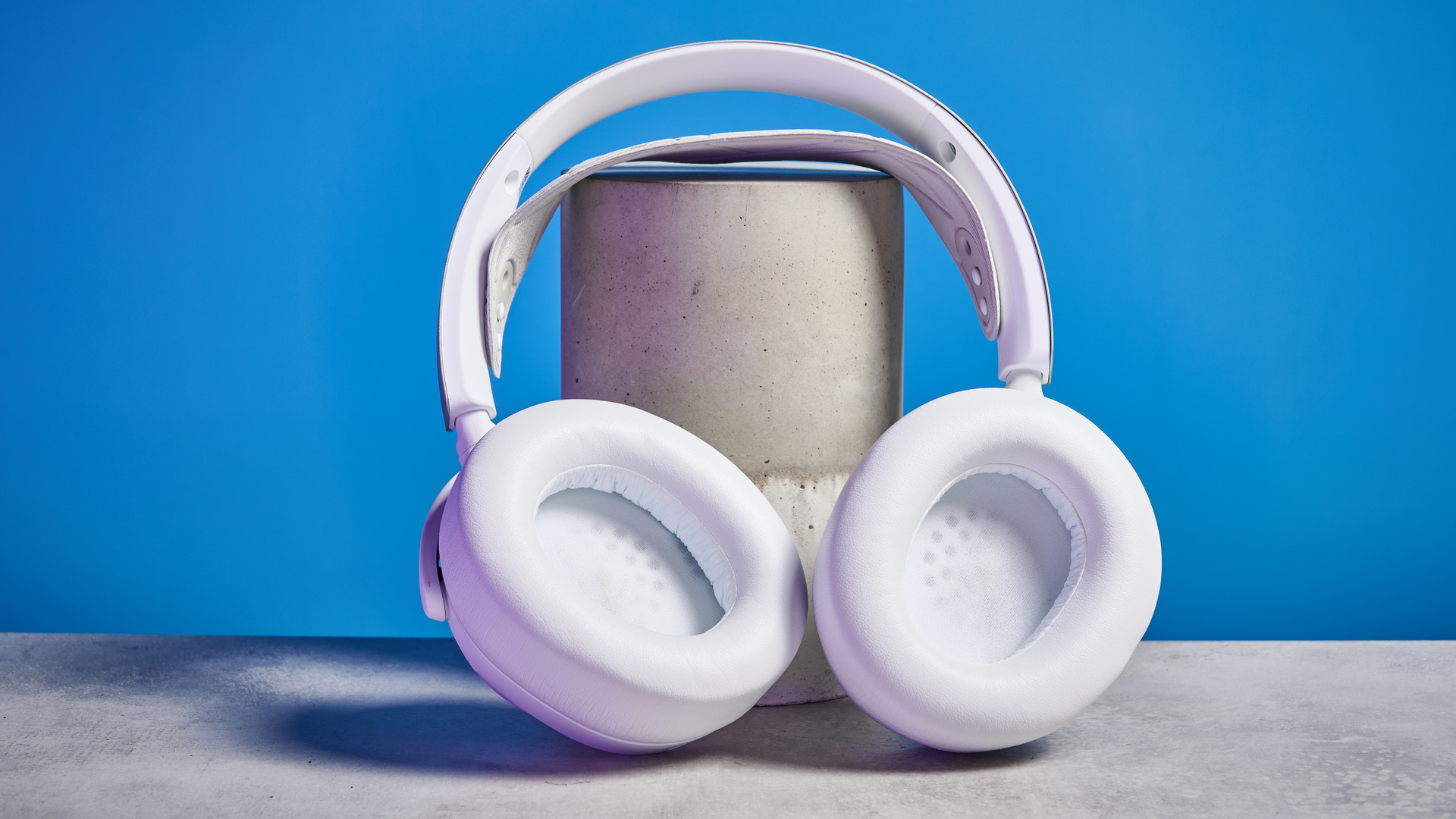 SteelSeries Arctis Nova Pro Wireless in white on a stone surface with a gentle purple reflection on the headset