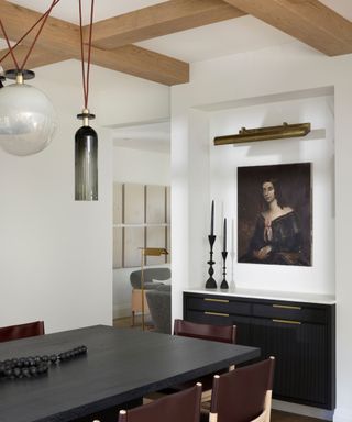 dining room with black table and artworks with pale wood beams and pendant lights