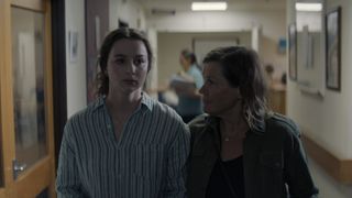 Tara Catton in a blue top as Grace and Robyn Malcolm in a dark top as Penny stand together in a corridor in After The Party.