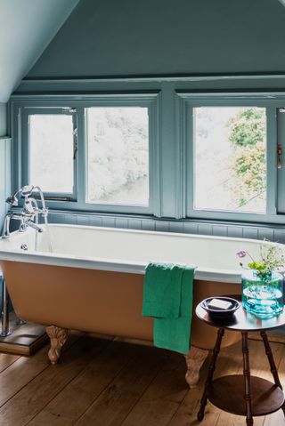 A suede coloured bath on a wooden floor in front of small windows