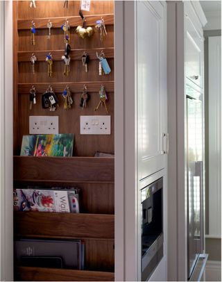 A rack for keys, magazines and plug sockets built in to a cabinet in a white kitchen