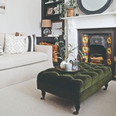A small living room with a cream sofa and a green velvet ottoman used as a coffee table with a tray on top