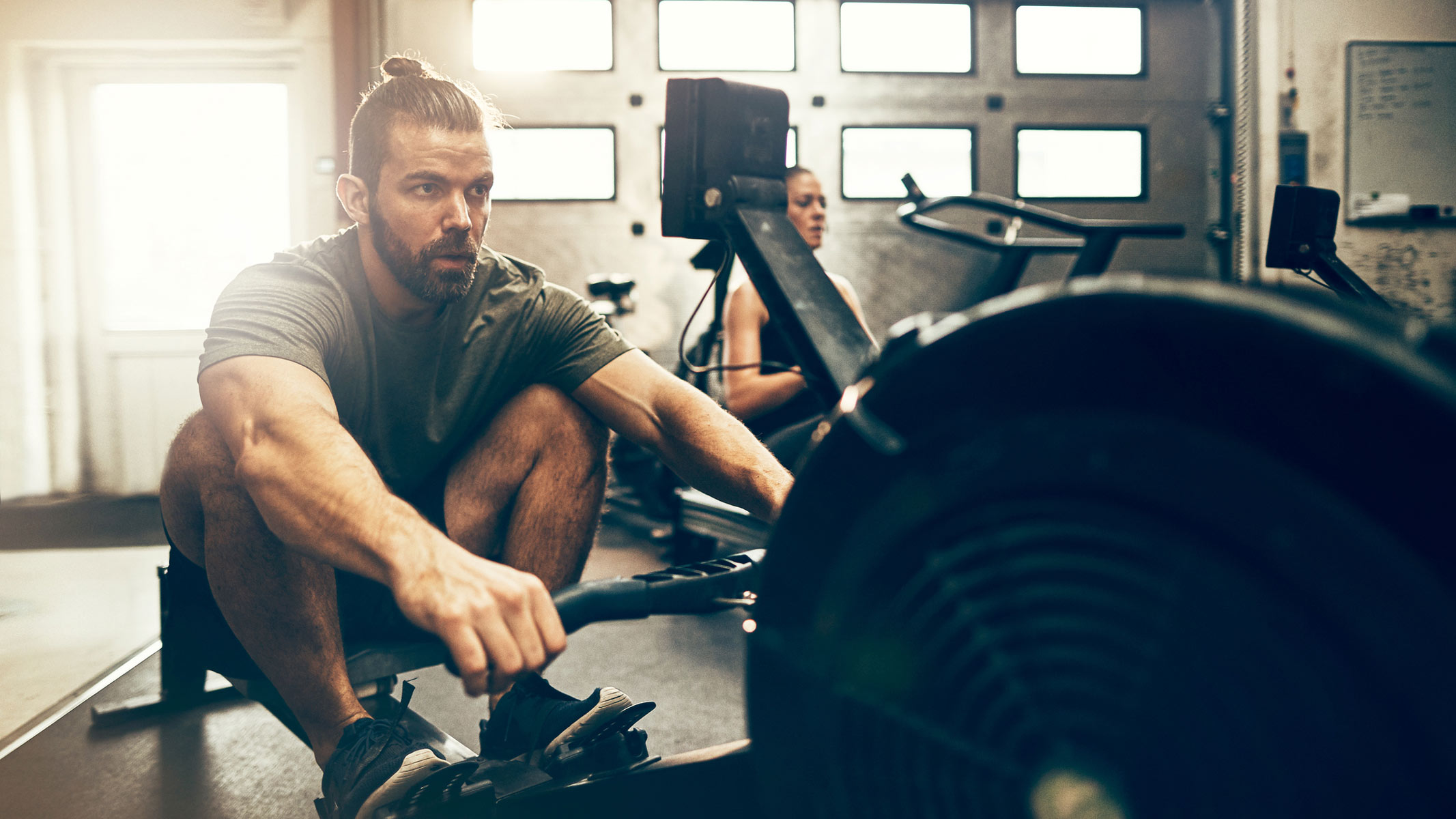 A man working out on a rowing machine while looking at his workout stats at the adjacent monitor