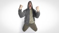 A man (Devin Townsend) wearing a hoodie, on his knees, fists clenched, screaming in despair, against a white background