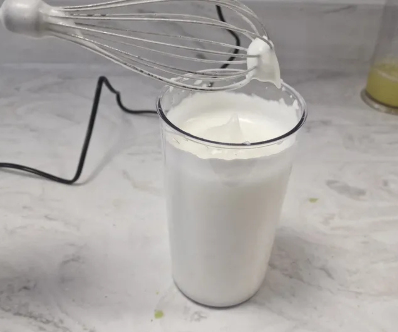 An electric hand whisk being held over a container of whipped cream.