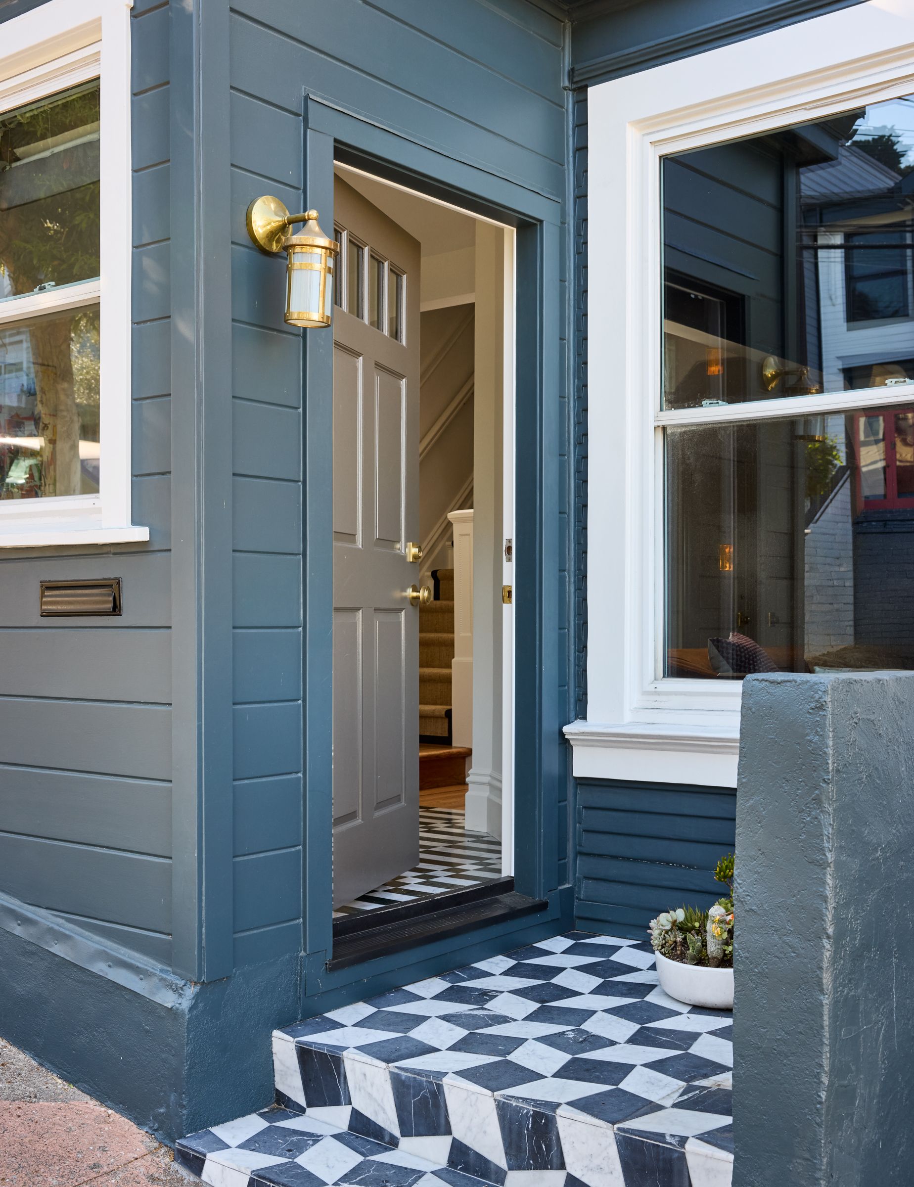 A front doorway with playful monochrome patterned tiles, and a brass wall light.