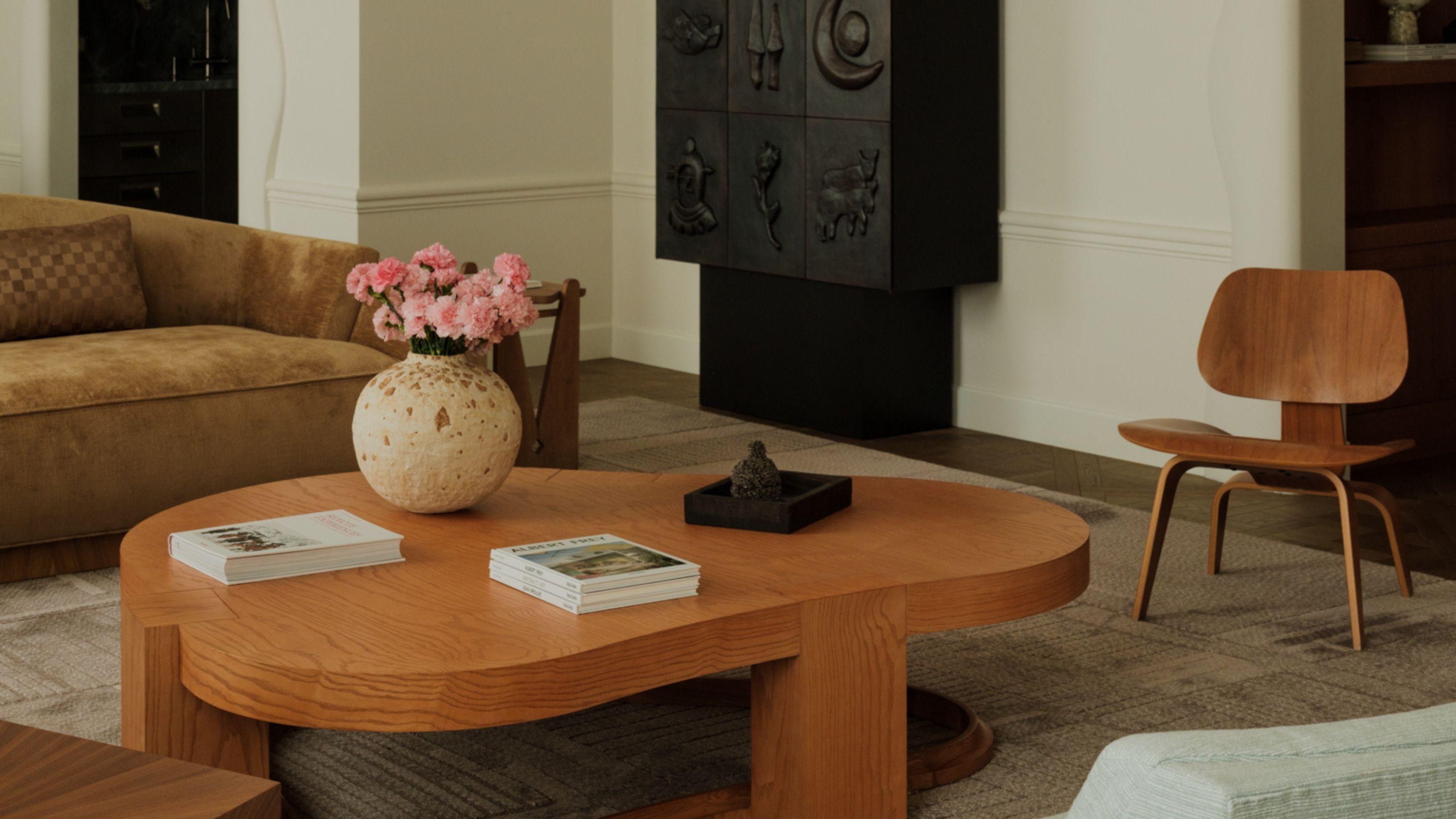 Close-up image of a living room with a beige rug, an abstract wooden coffee table, a brown sofa, and a wooden accent chair.