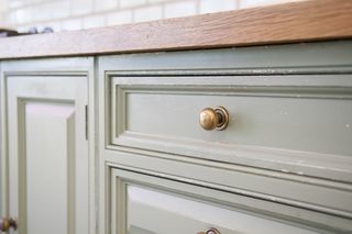 A close up of a green kitchen unit with green drawers and small gold handles.