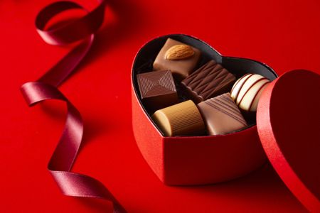 heart-shaped box of chocolates with a red ribbon against a red background