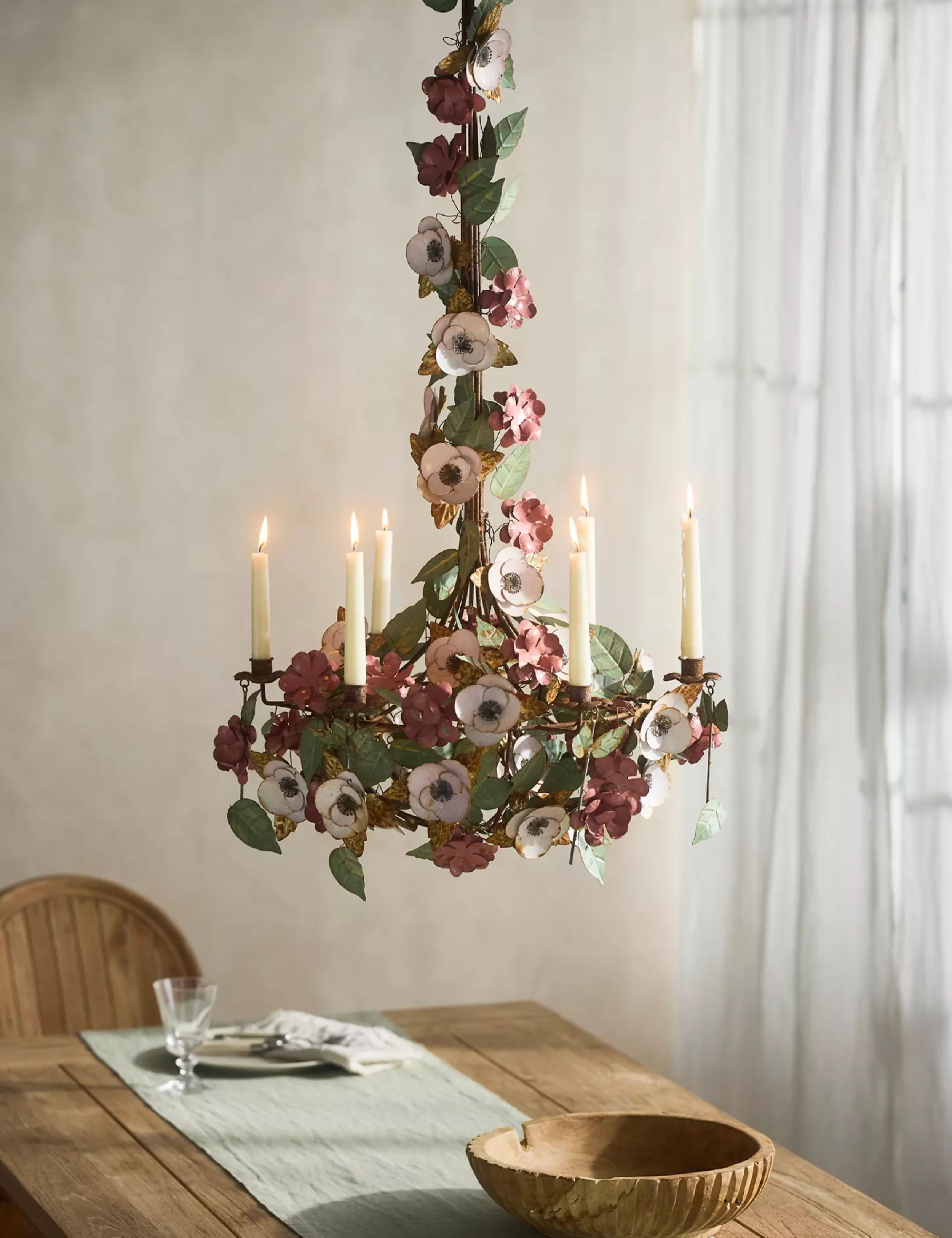 Anthropologie candle chandelier pictured in a dining room with wooden dining furniture and sheet curtains