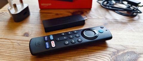 The Amazon Fire TV Stick next to its remote and box on a wooden table.
