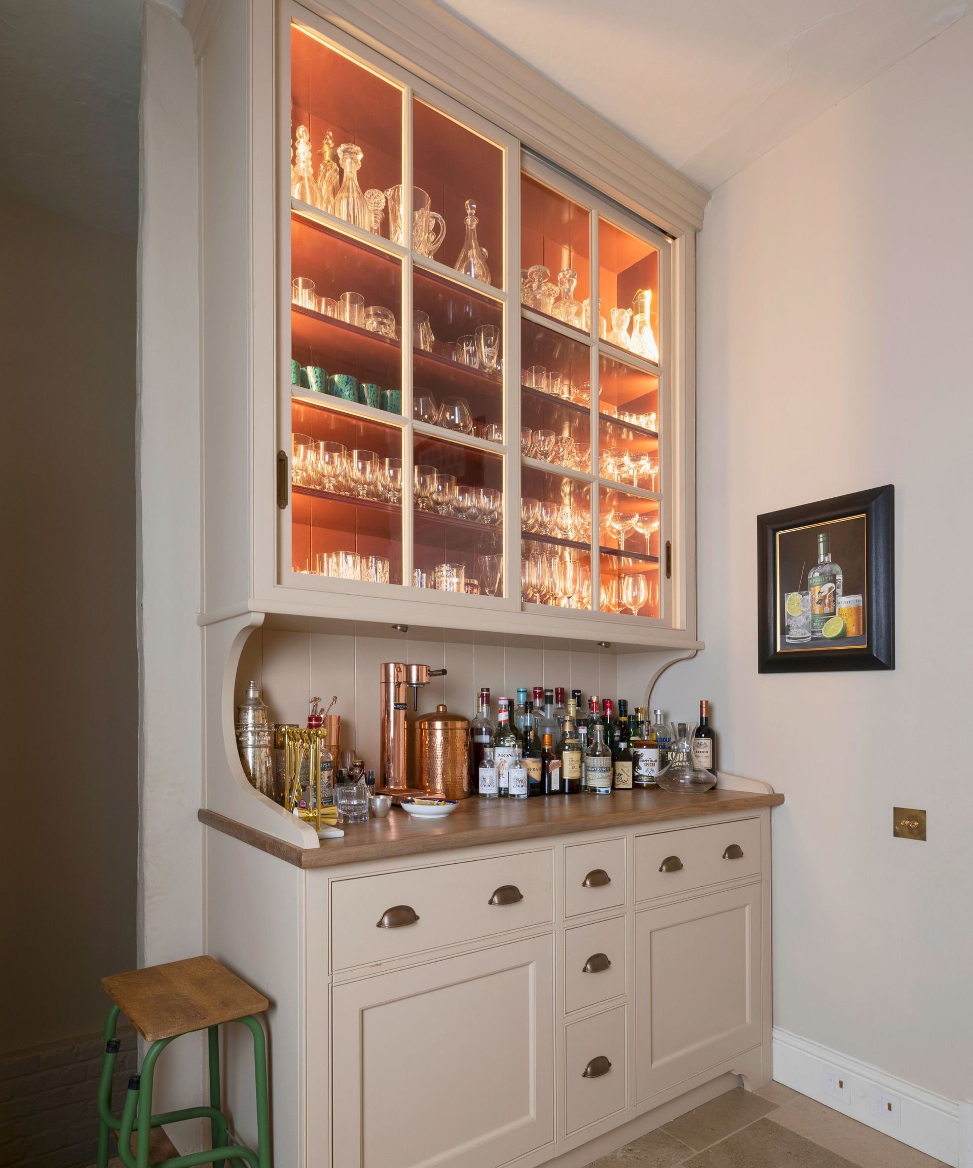 A cream kitchen bar with back lit glass storage in a glass cabinet