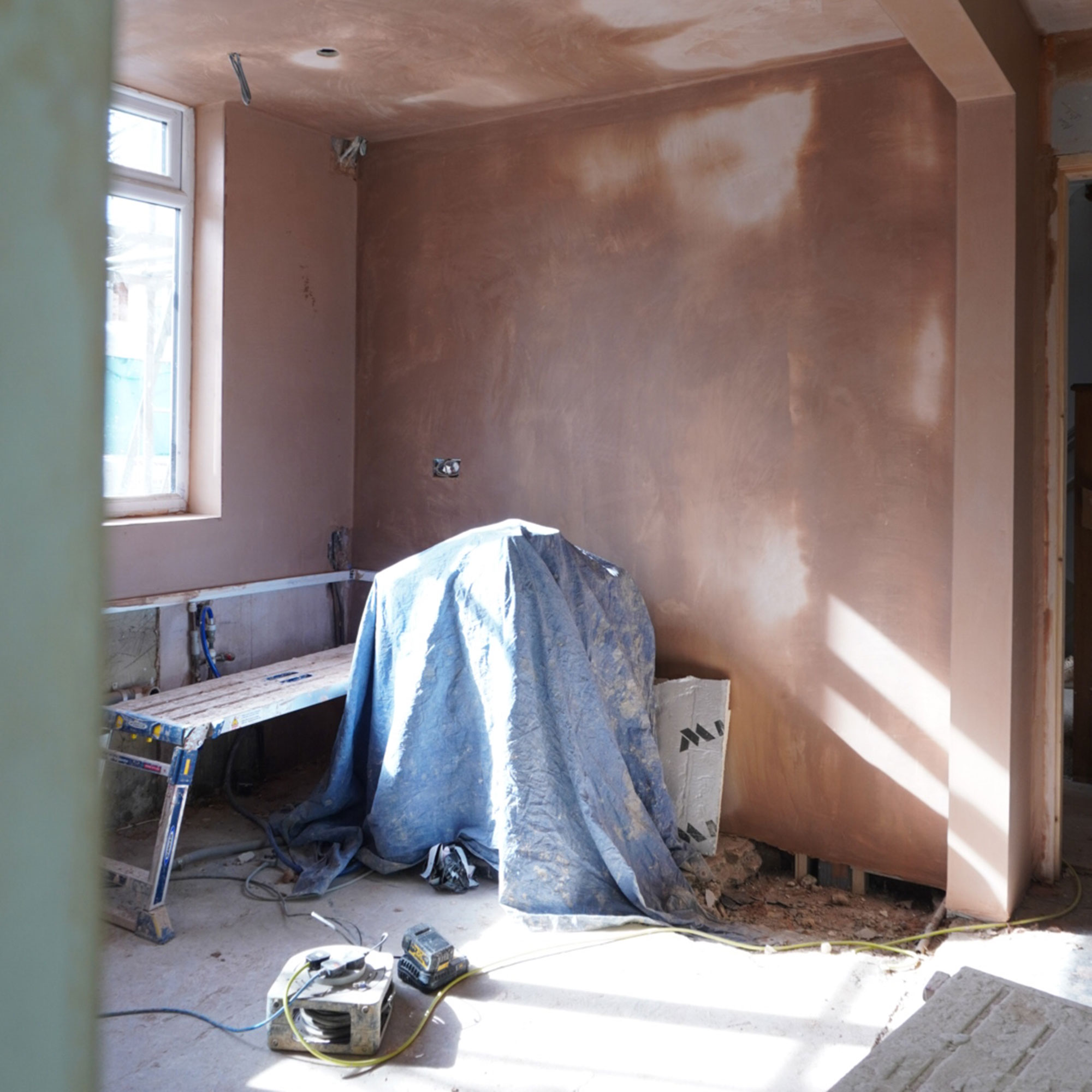 Room mid renovation with plastered walls and paint-splattered bench