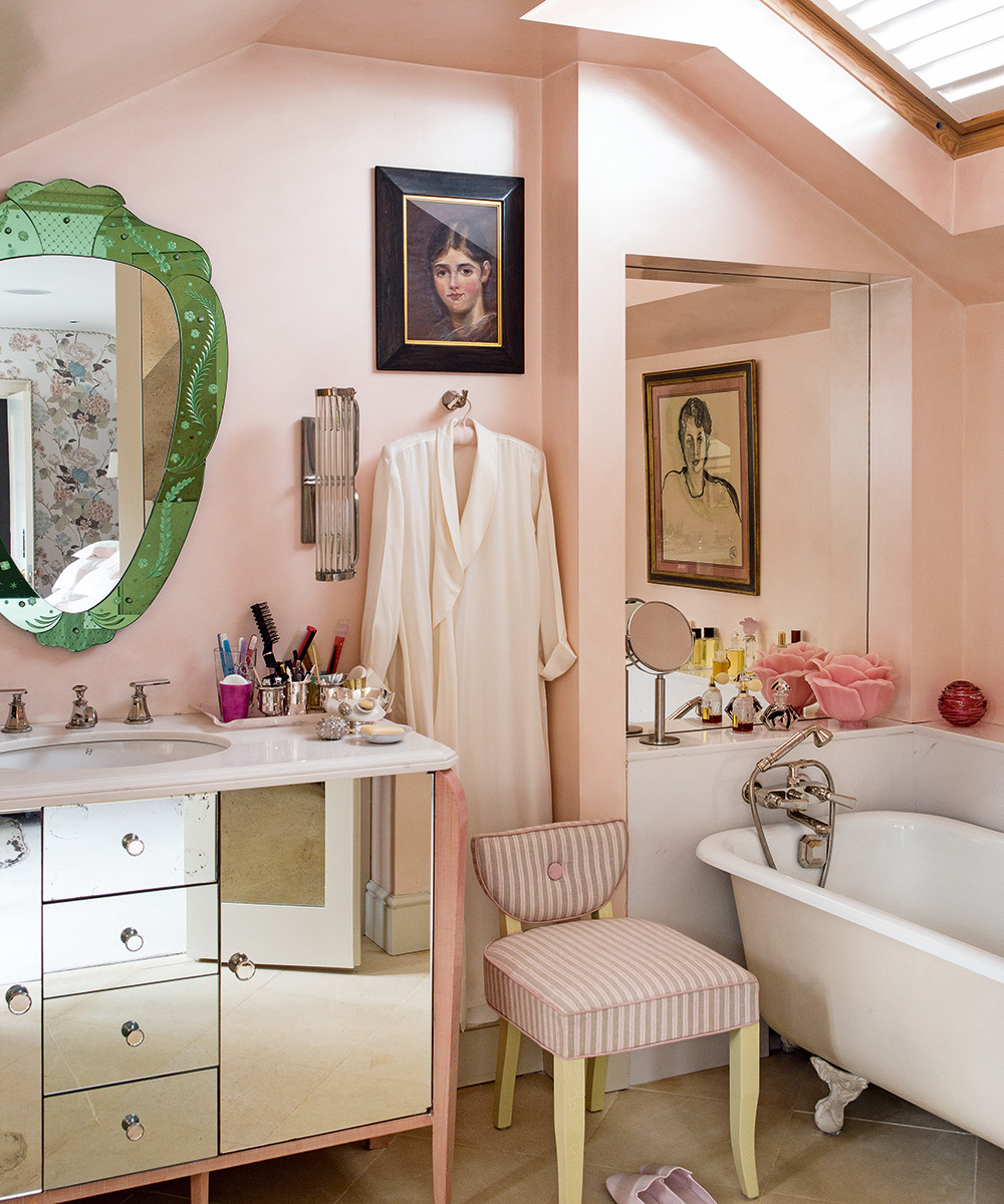 An example of bathroom paint ideas showing a pink bathroom with a mirrored vanity unit, a white rolltop bath and a pink and white striped upholstered chair