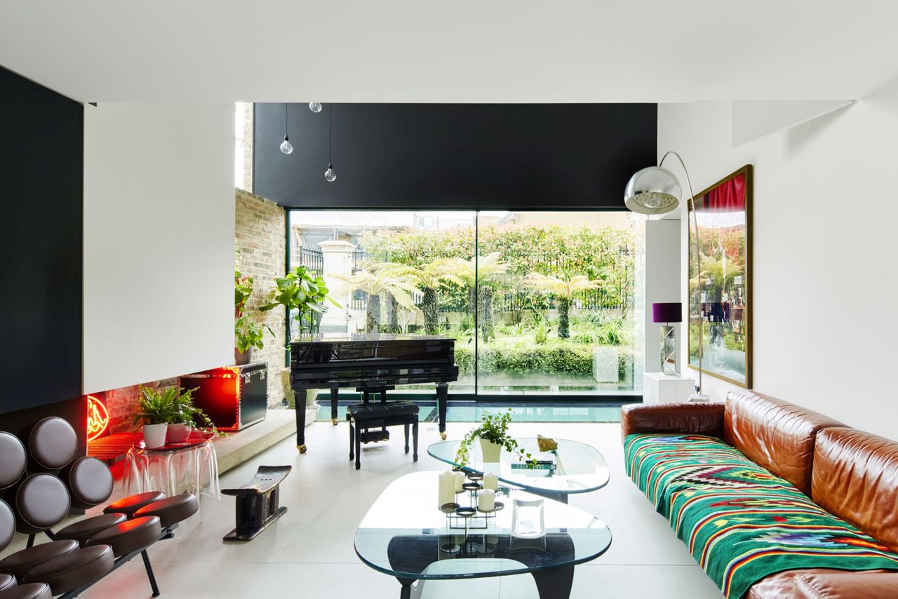 The living room has a glazed wall and piano inside with large screen tv