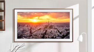Samsung's The Frame 2023 TV on a wall, with a lamp and window nearby, showing a photo of the Paris skyline on the screen