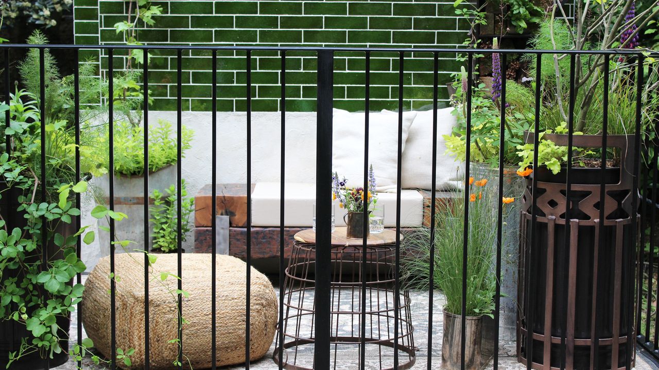 Small balcony garden with green subway tiles on wall and black railings