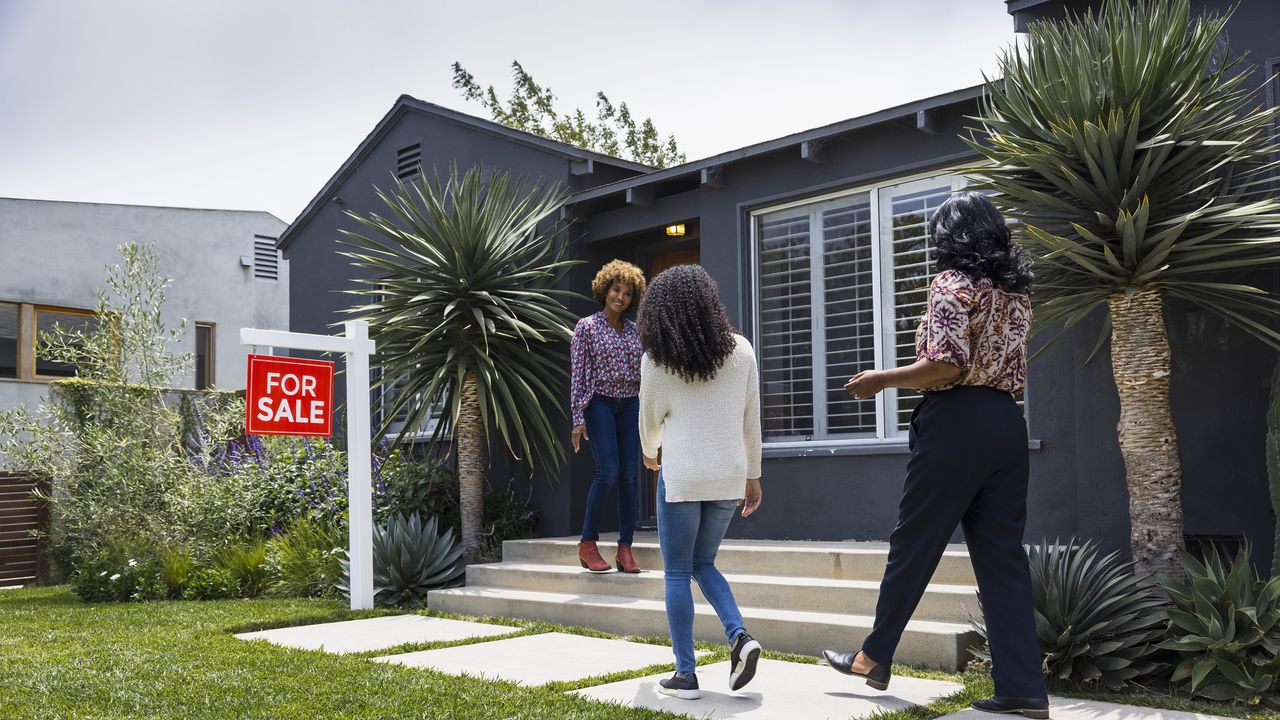 Real estate agent greets customers while standing outside a house for sale.