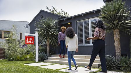 Real estate agent greets customers while standing outside a house for sale.