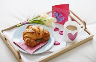 A Valentine's/Mother's Day breakfast with a croissant, a mug of tea, a homemade card, and flowers.