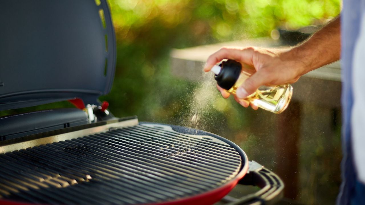 Close up on man&#039;s hand spraying oil on barbecue gas grill to season the grill