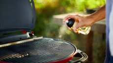 Close up on man's hand spraying oil on barbecue gas grill to season the grill