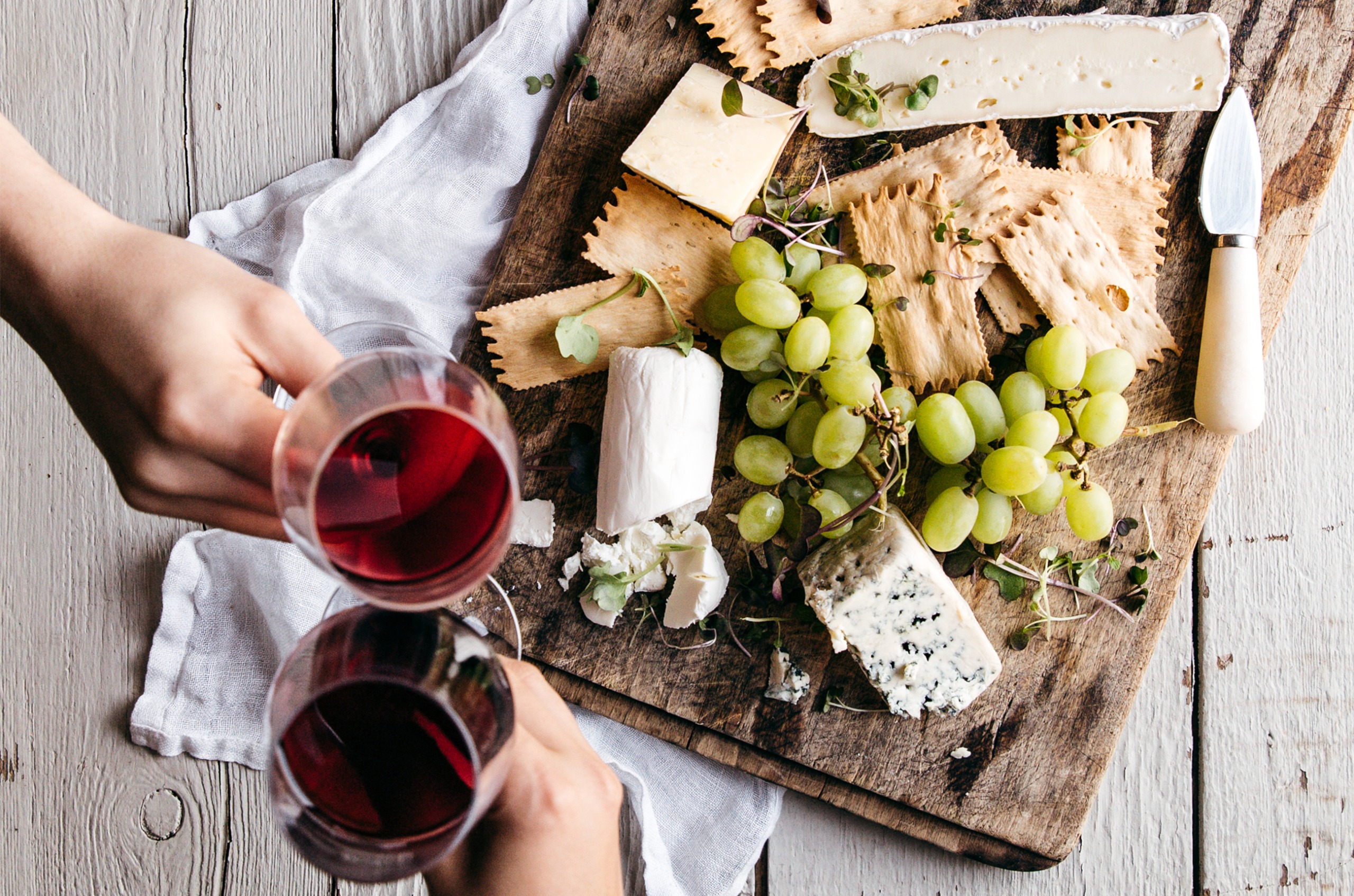 A cheeseboard with different types of cheese and grapes, and two glasses of red wine