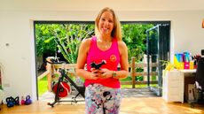 Woman stands holding massage gun in domestic setting