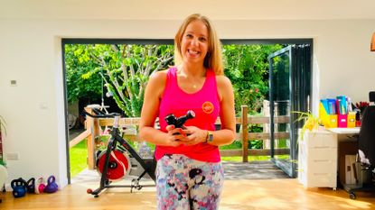 Woman stands holding massage gun in domestic setting