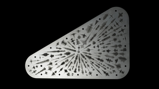 Image of one side of the commerative plate which is a silver-color, against a black background. The plate appears to have lots of symbolic markings across it and is the shape of a right-angled triangle