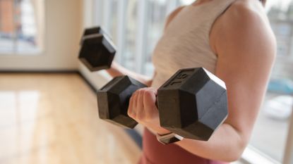 Low Section Of Woman Exercising With Dumbbells At Home
