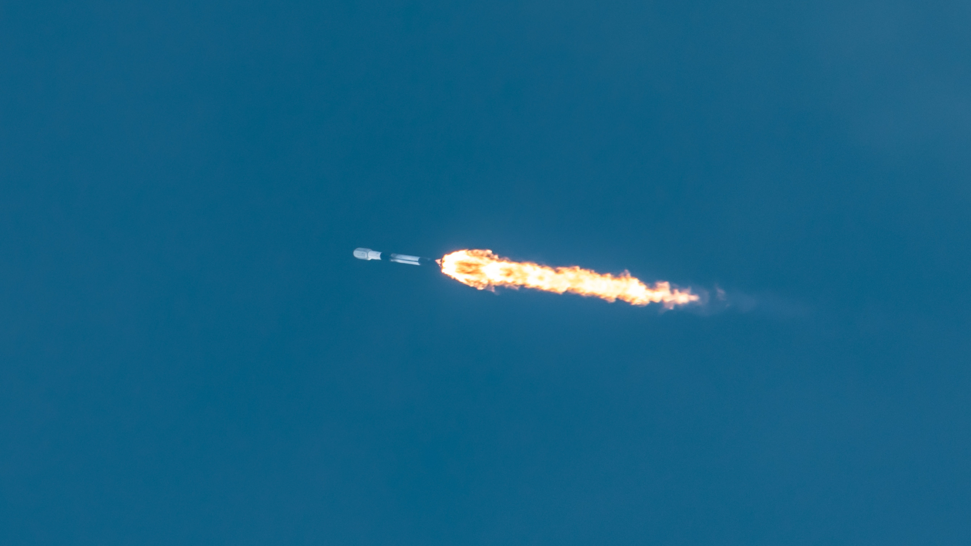 a white and black rocket streaks into a blue sky, as seen from below,