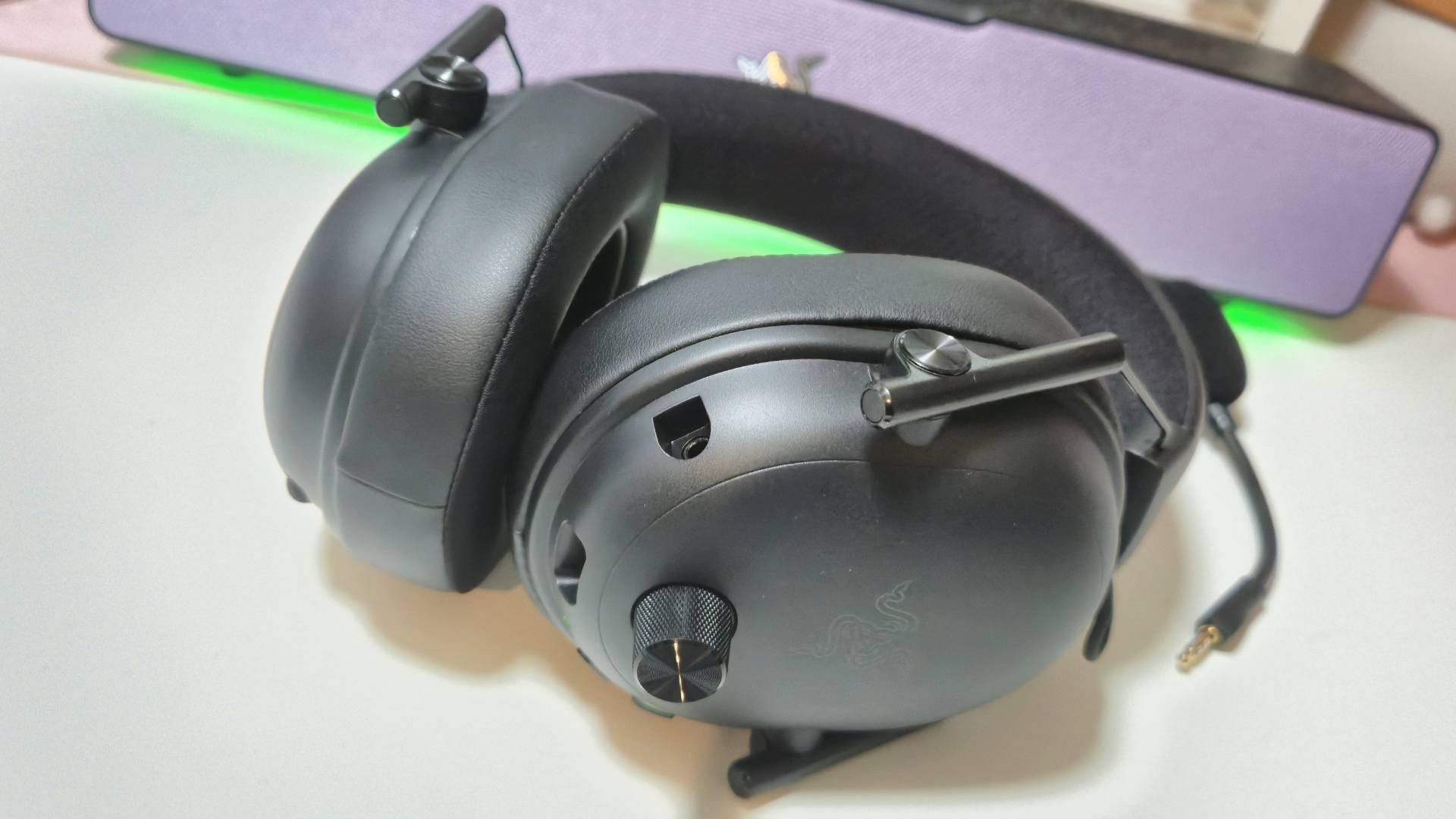 Photo by Rosalie Newcombe of the Razer BlackShark V3 sitting on a white desk with a green glow behind it.